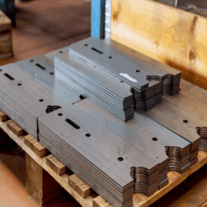 Stacked laser cut steel parts with rounded corners and slot holes on a wooden pallet
